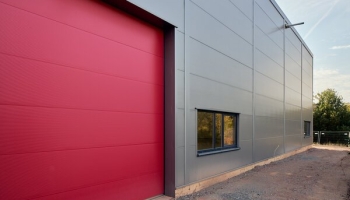 Ein Himbeerrotes Sektionaltor vor einer Stahlhalle - eine farbenfrohe und ansprechende Option für den Eingangsbereich.